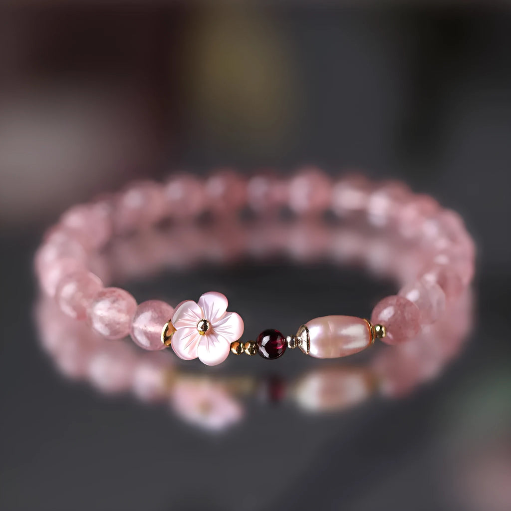 Women's strawberry quartz crystal bracelet with a floral peach blossom design on a wrist.