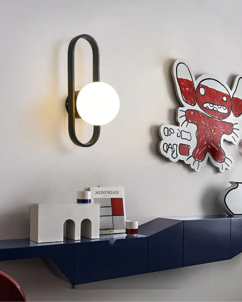Minimalist modern wall lamp with glass shade and iron body in black finish, mounted on a wall.