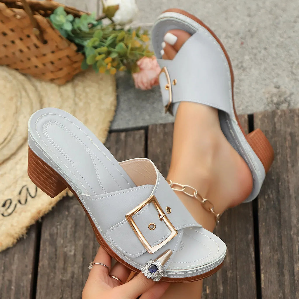 Women's black chunky heel slippers with a round toe and metal buckle on a light background.