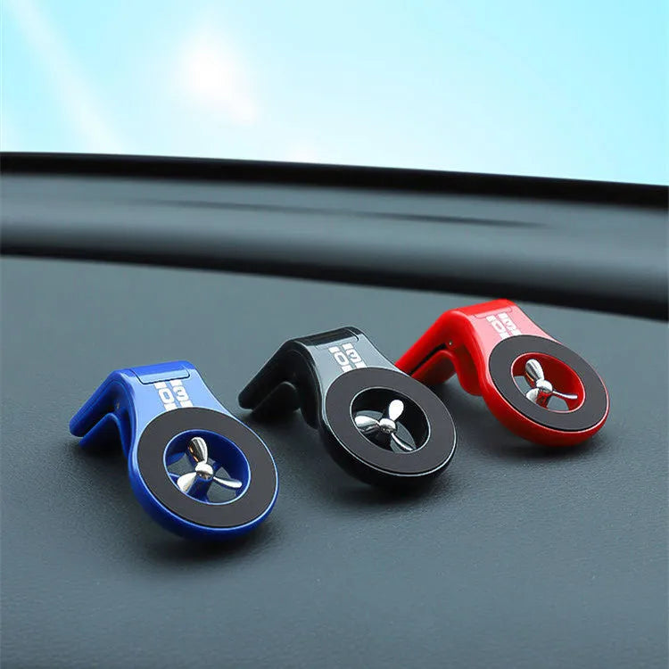 Black magnetic car phone holder clipped to a car air vent, showing a smartphone attached and the included fragrance slice.