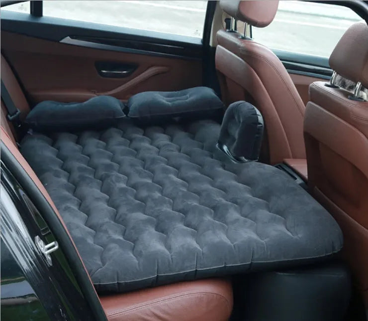 Black inflatable car bed with flocked surface and two pillows, shown inside a vehicle.