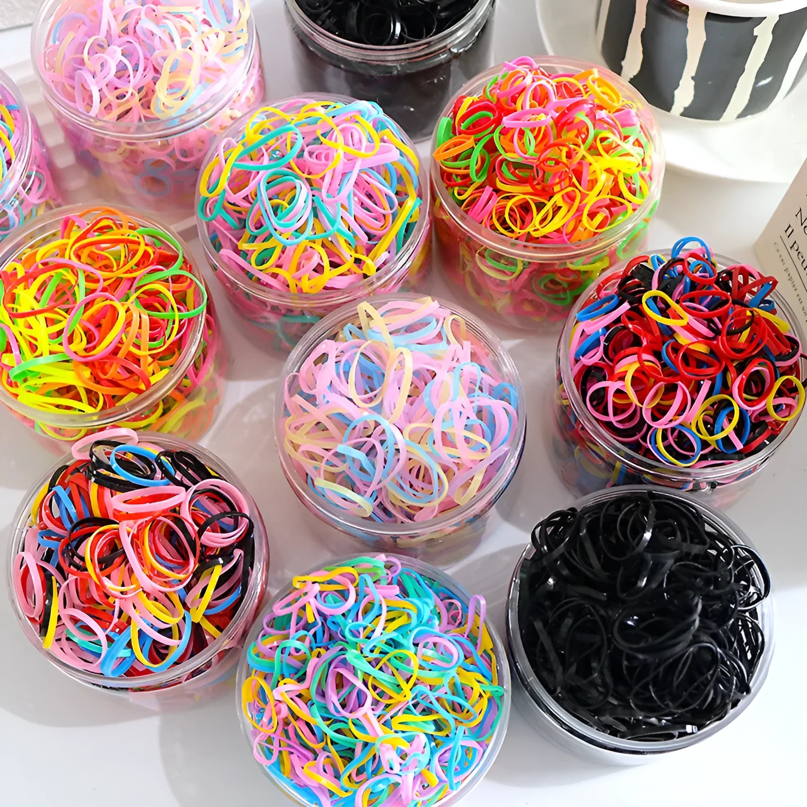 Pack of multicoloured thin TPU baby hair ties stored in a clear reusable plastic container.