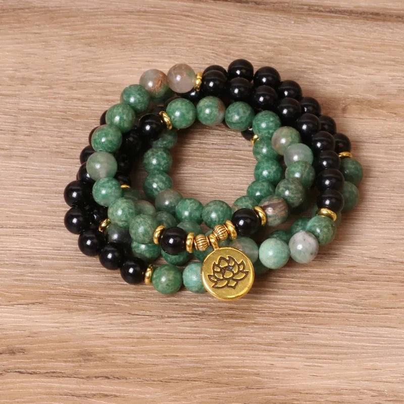 Green and black elastic beaded bracelet with metallic alloy charm details on a wrist.