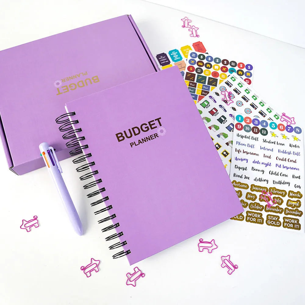 Purple coil-bound budget notebook open showing monthly planning pages with financial stickers and paper clips