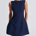 A woman wearing a slim-fitting black backless sleeveless summer dress with a high waist and short skirt.
