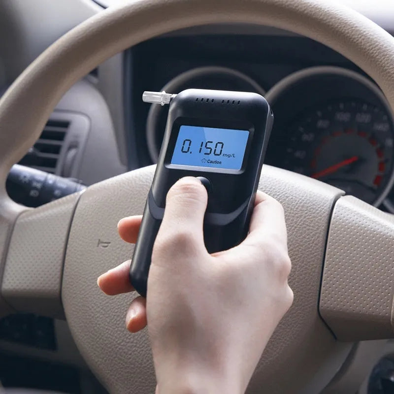 Black portable household alcohol breath tester with LCD screen on a dark background.