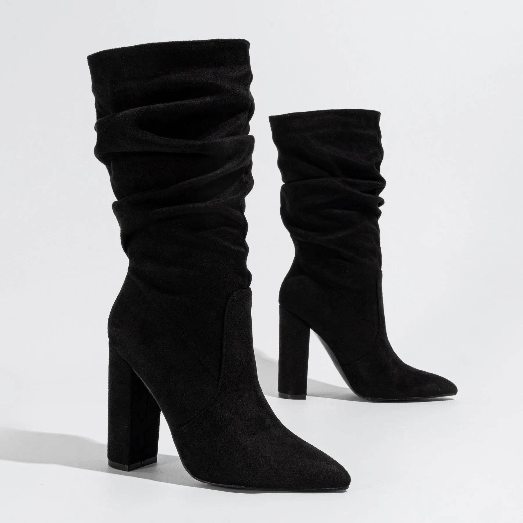 Women's black suede knee-high boots with a chunky high heel and pointed toe on a plain background.