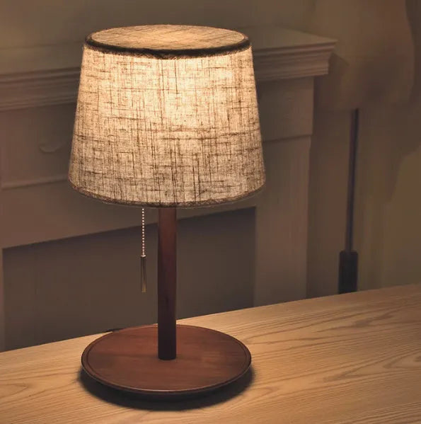 Walnut-coloured solid wood bedside lamp with white fabric shade on wooden table
