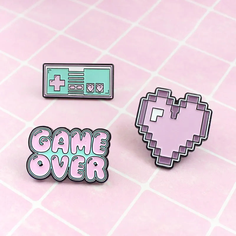 Stereo game console metal badge in protective OPP packaging, shown in one of three colour variants.