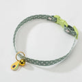 Green adjustable pet collar with a metal bell and a pink bow tie attached, shown on a small dog.