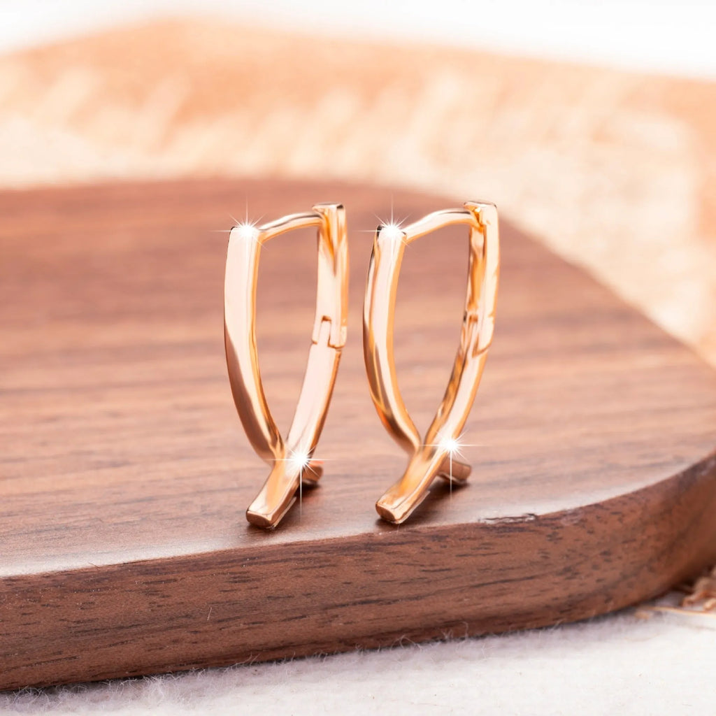 A pair of rose gold cross-shaped earrings made from copper on a white background.