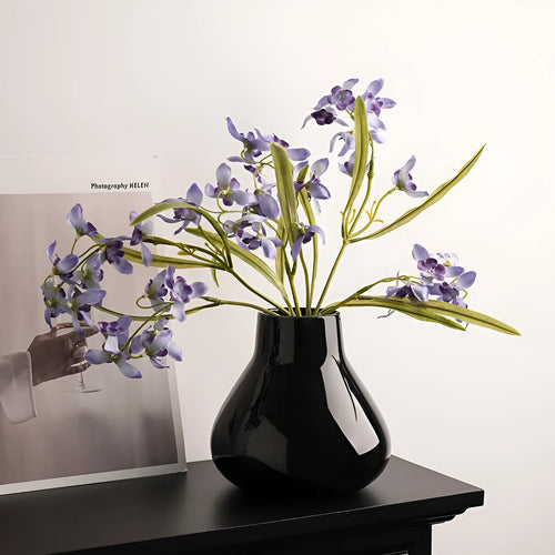 Ceramic round belly vase in black or white with artificial orchid stems on wooden surface