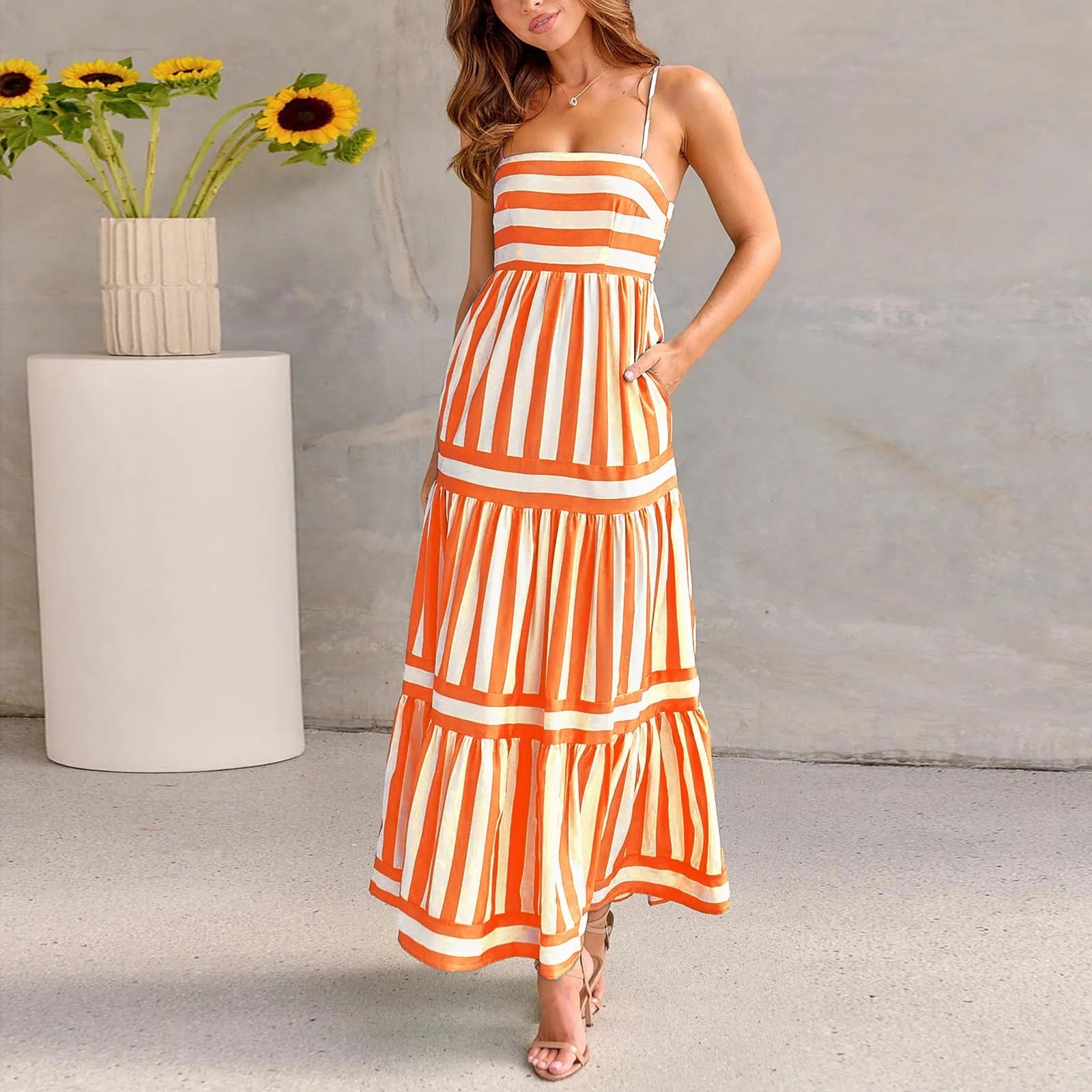 A woman wearing a striped backless suspender summer dress with a square neckline and side pockets.