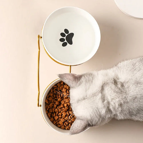 White ceramic pet bowl with cat paw print design on a black iron frame stand with cat ear details.