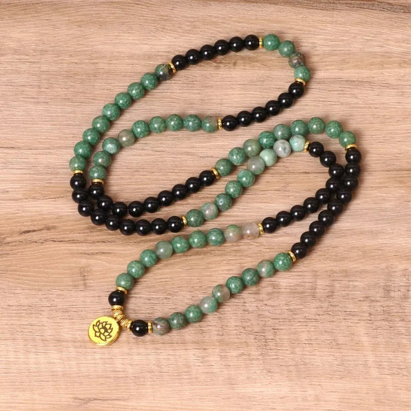 Green and black elastic beaded bracelet with metallic alloy charm details on a wrist.