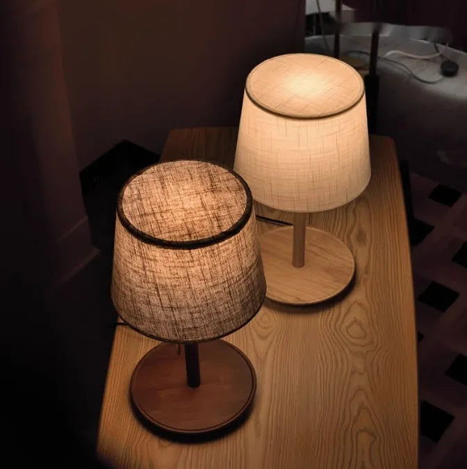 Walnut-coloured solid wood bedside lamp with white fabric shade on wooden table