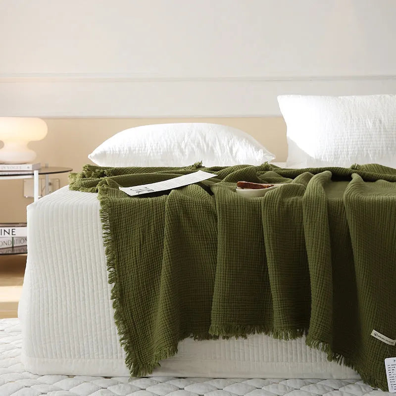 Four-layer gauze cotton tassel blanket in avocado green colour laid flat.
