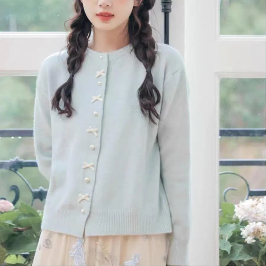 Women's solid colour cashmere cardigan with bow detail and pearl buttons on a hanger