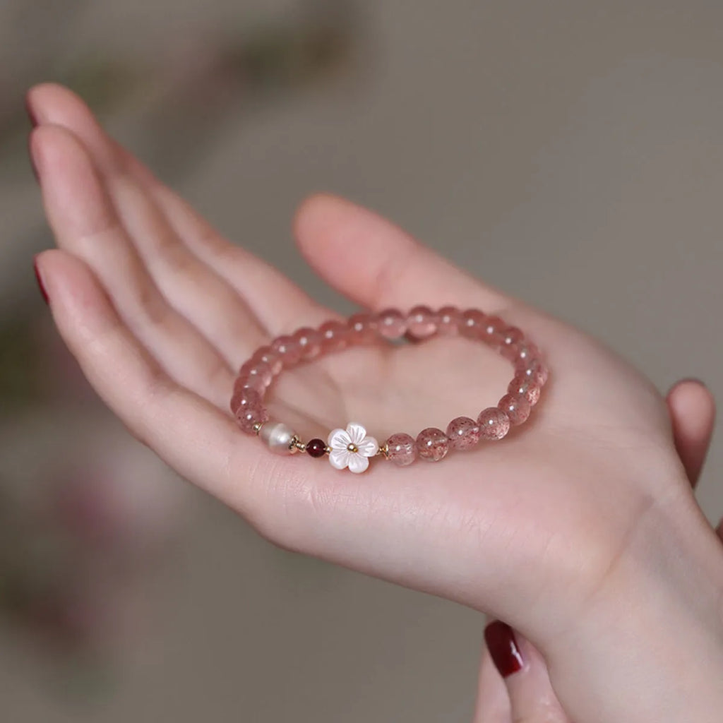 Women's strawberry quartz crystal bracelet with a floral peach blossom design on a wrist.