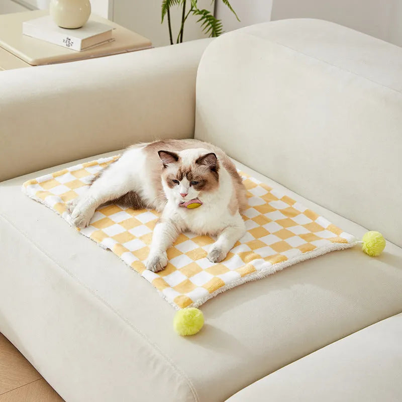 Green plaid pattern pet blanket with fur ball tassels on a sofa.