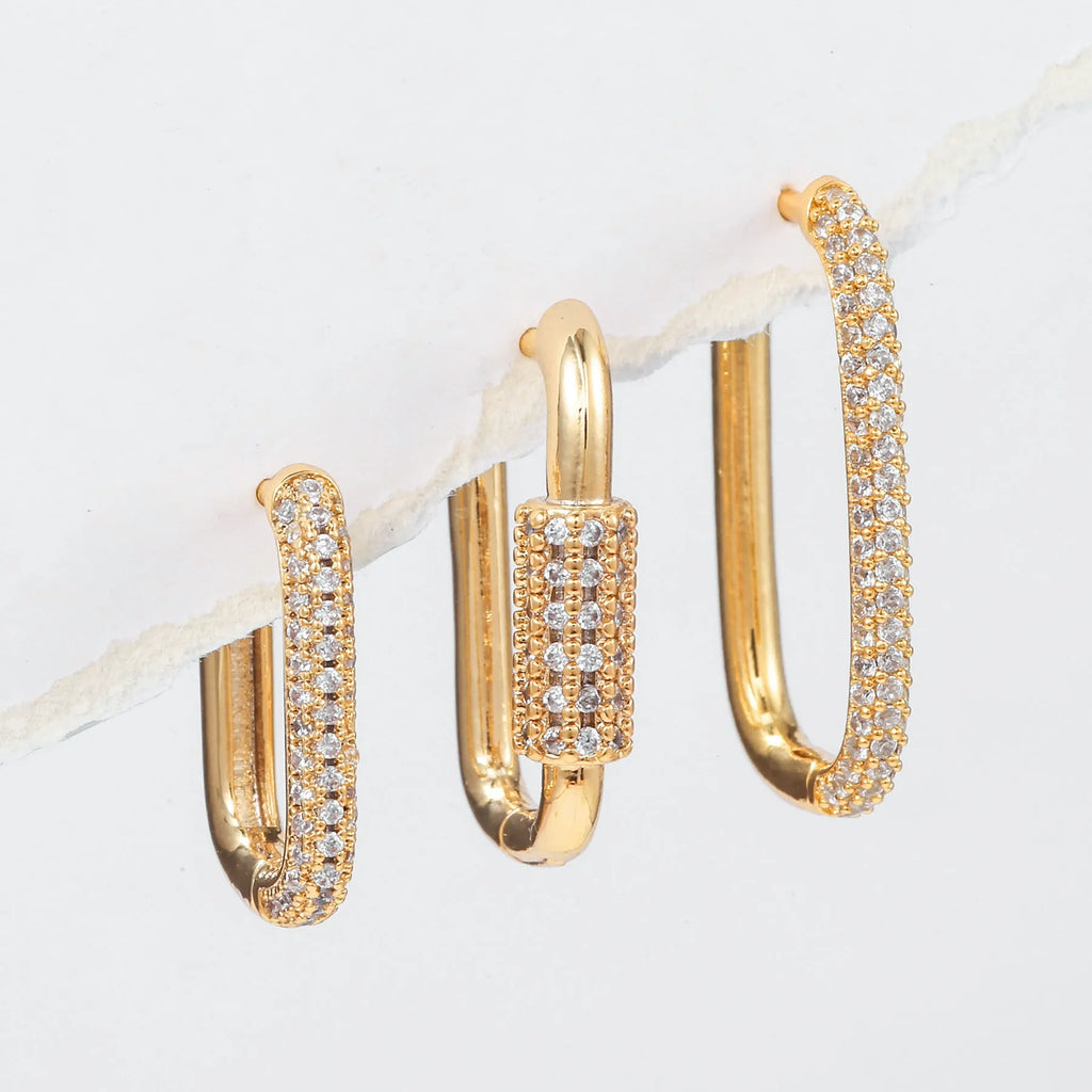 Three geometric square ear clips with inlaid zircon details in gold and white finishes on a grey background.