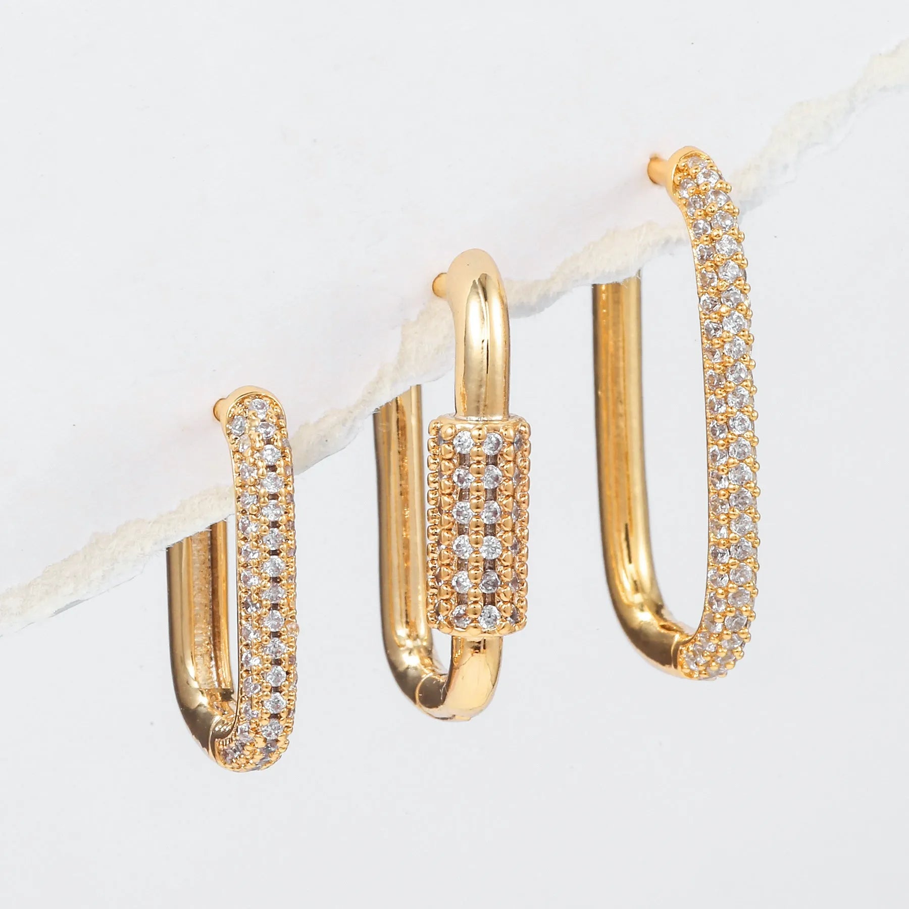 Three geometric square ear clips with inlaid zircon details in gold and white finishes on a grey background.
