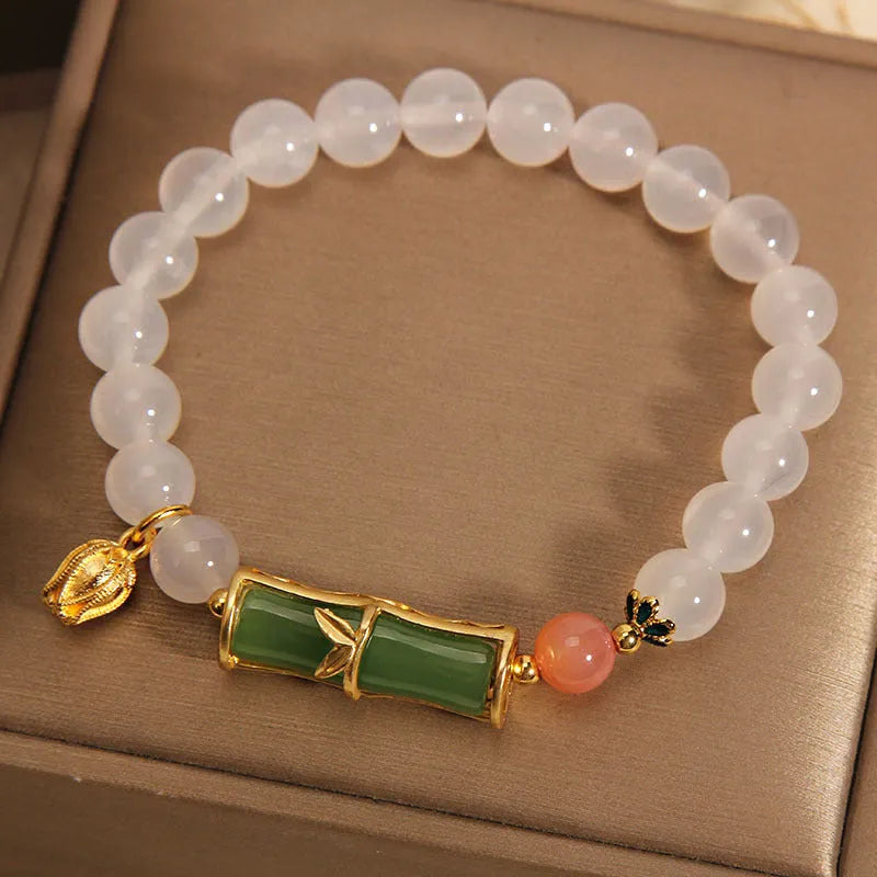 Women's bracelet with white agate bead and bamboo-shaped jade segments on a neutral background.