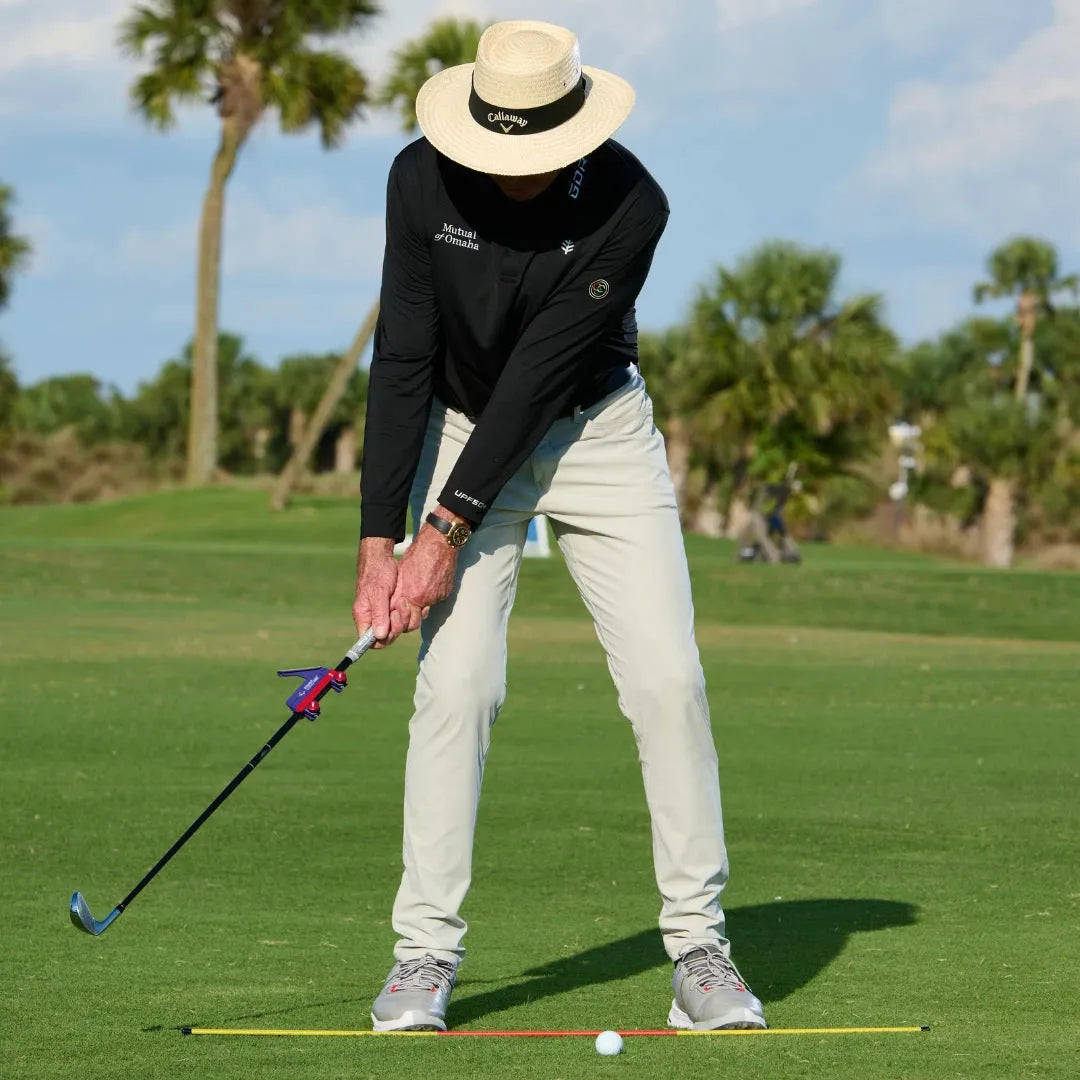 A plastic golf swing plane simulator training aid on a green background.