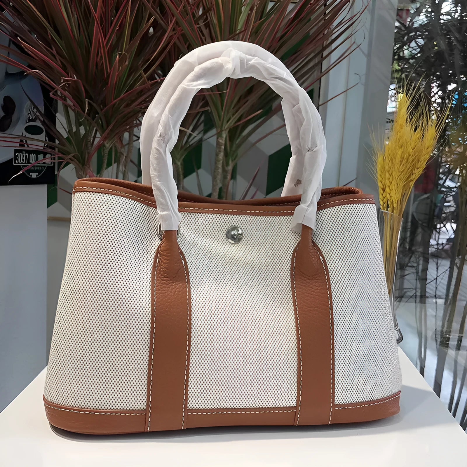 Women's canvas bucket tote bag with leather handles and detailing in black, shown with open top revealing internal zip pocket.
