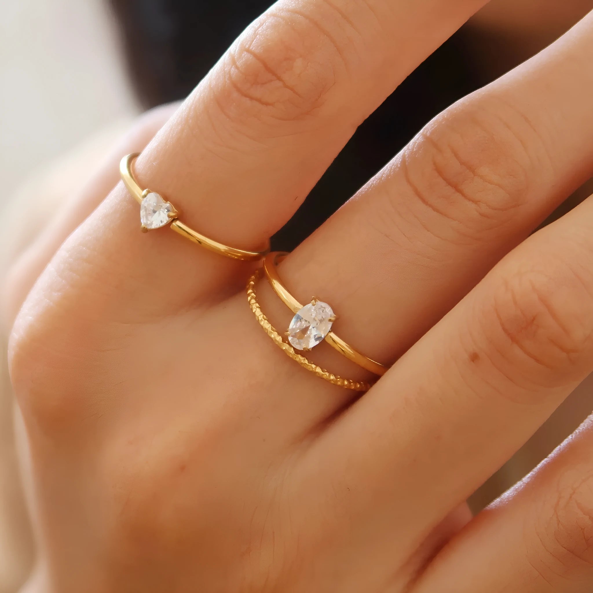 Golden electroplated stainless steel love heart ring and oval ring for women on a plain background.