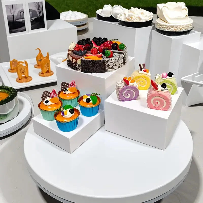 Six white plastic cube dessert display stands in graduated sizes from 3 to 8 centimetres.