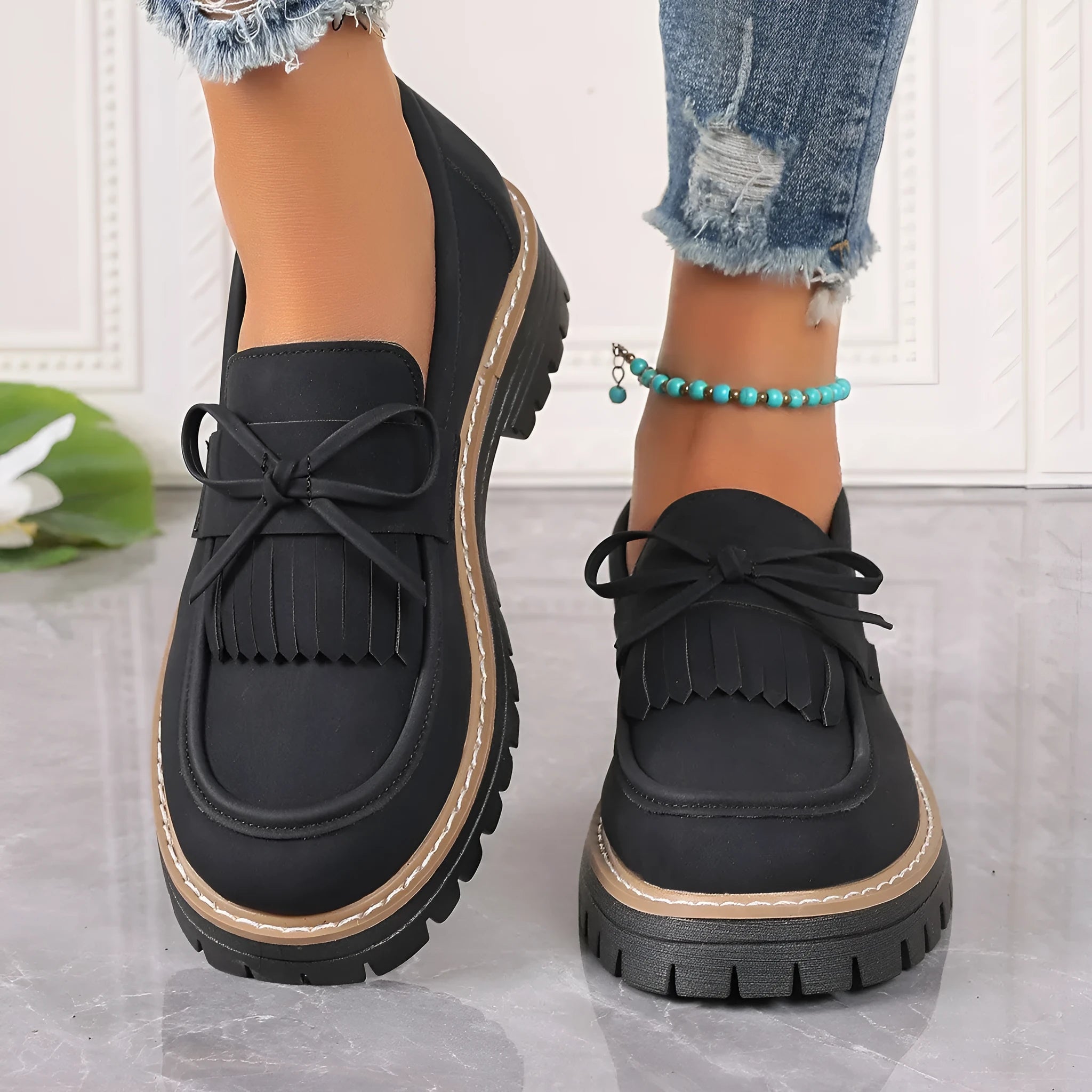 Black and brown women's loafers with tassel and bowknot decoration on a chunky low heel.