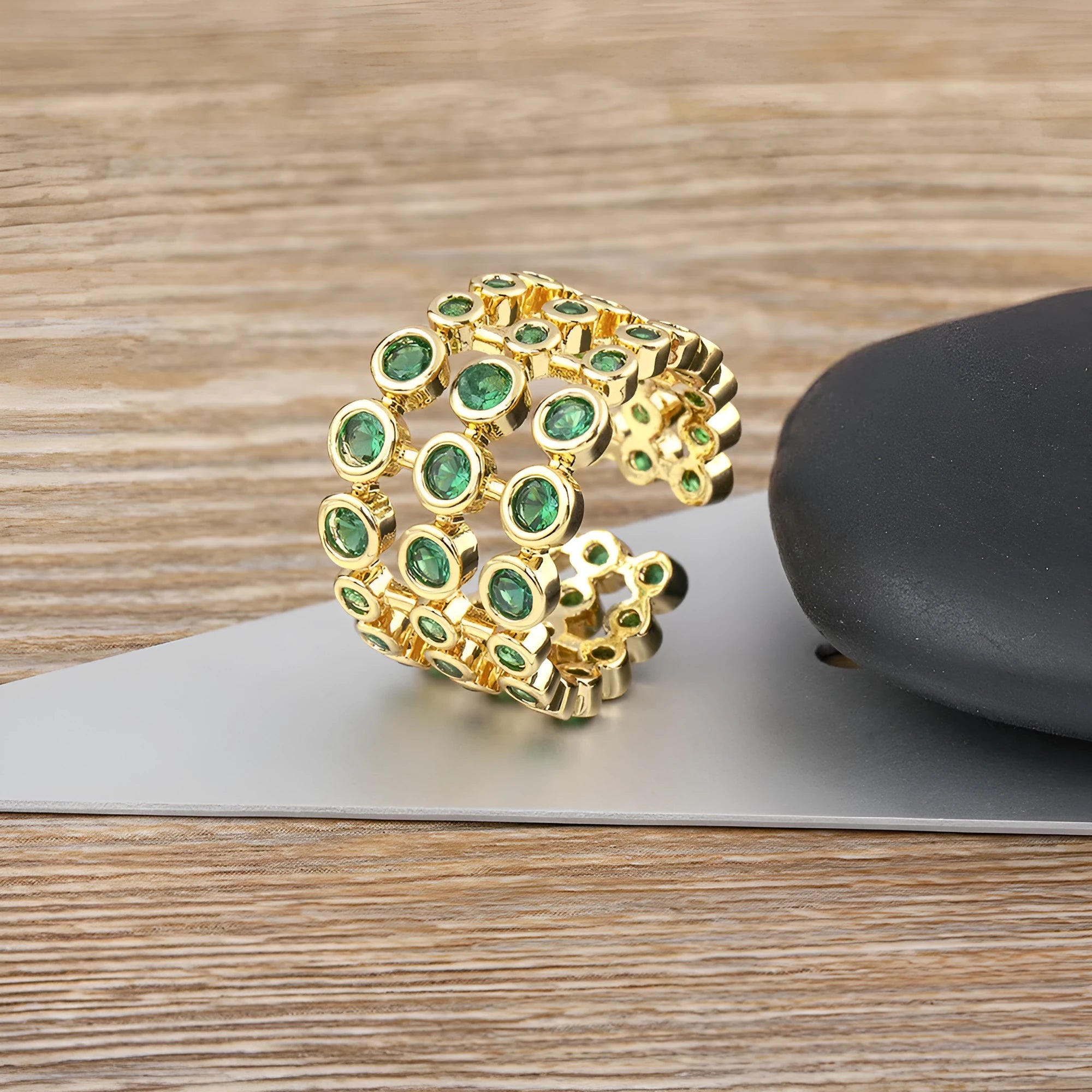 Gold-coloured wide band copper ring with large green zircon stones in a three-layer setting.