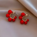 A pair of red alloy drop earrings featuring a small bell charm on a stud fitting.
