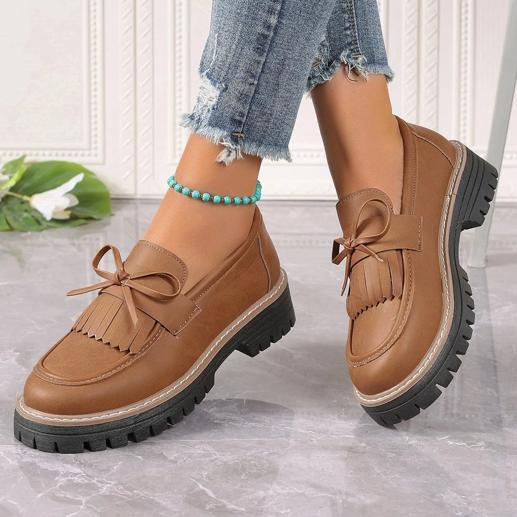 Black and brown women's loafers with tassel and bowknot decoration on a chunky low heel.
