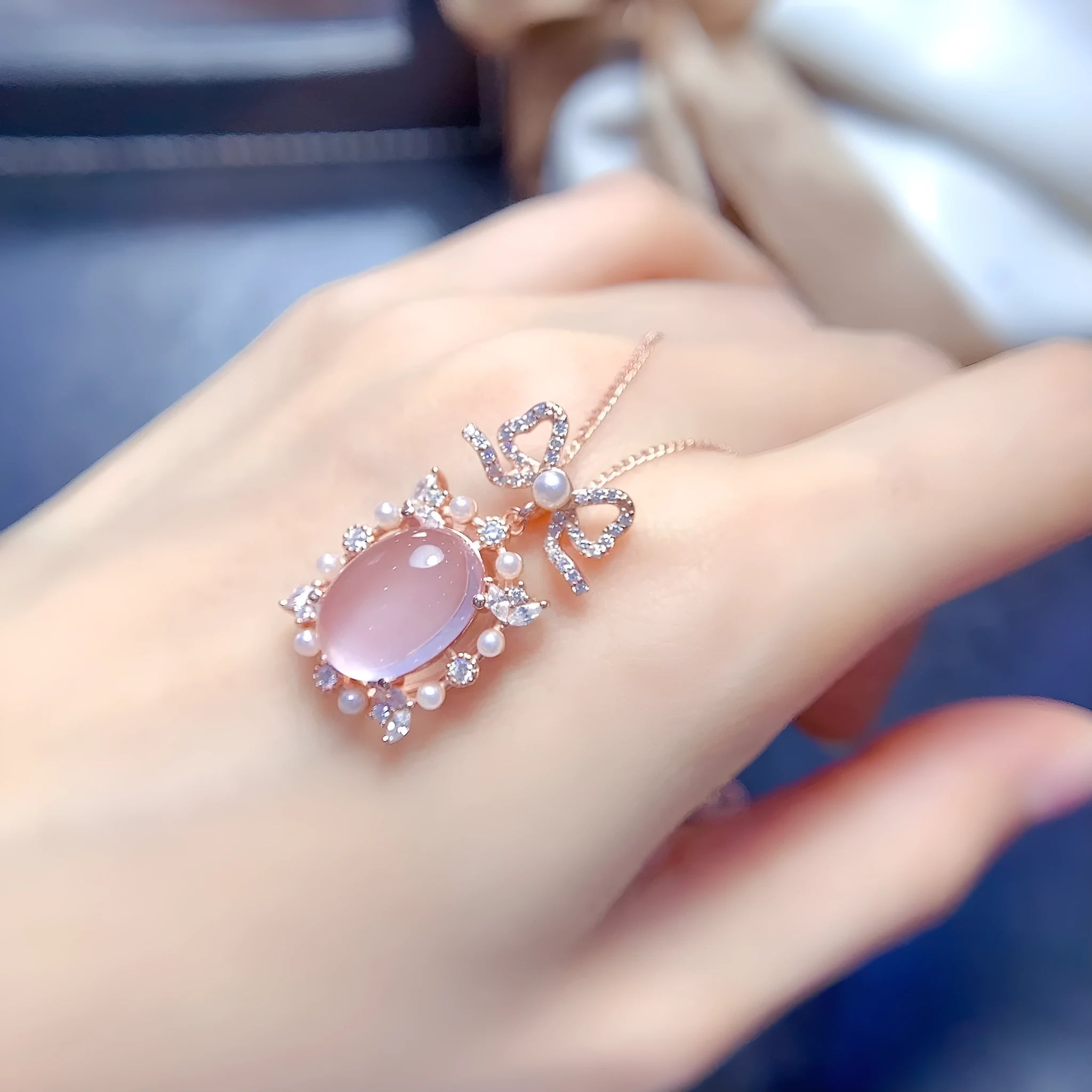 Close-up of a geometric silver pendant with a pink rose quartz stone and rose gold plating on a chain.
