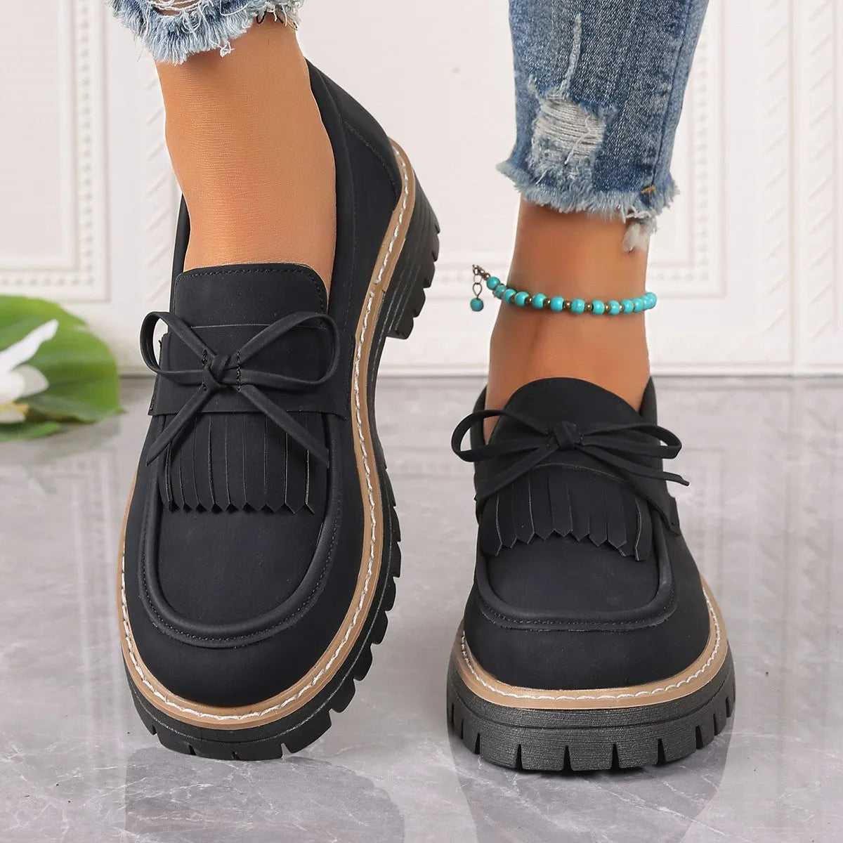 Black and brown women's loafers with tassel and bowknot decoration on a chunky low heel.