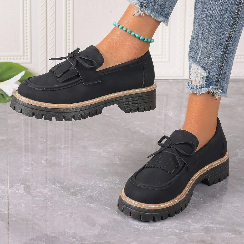 Black and brown women's loafers with tassel and bowknot decoration on a chunky low heel.
