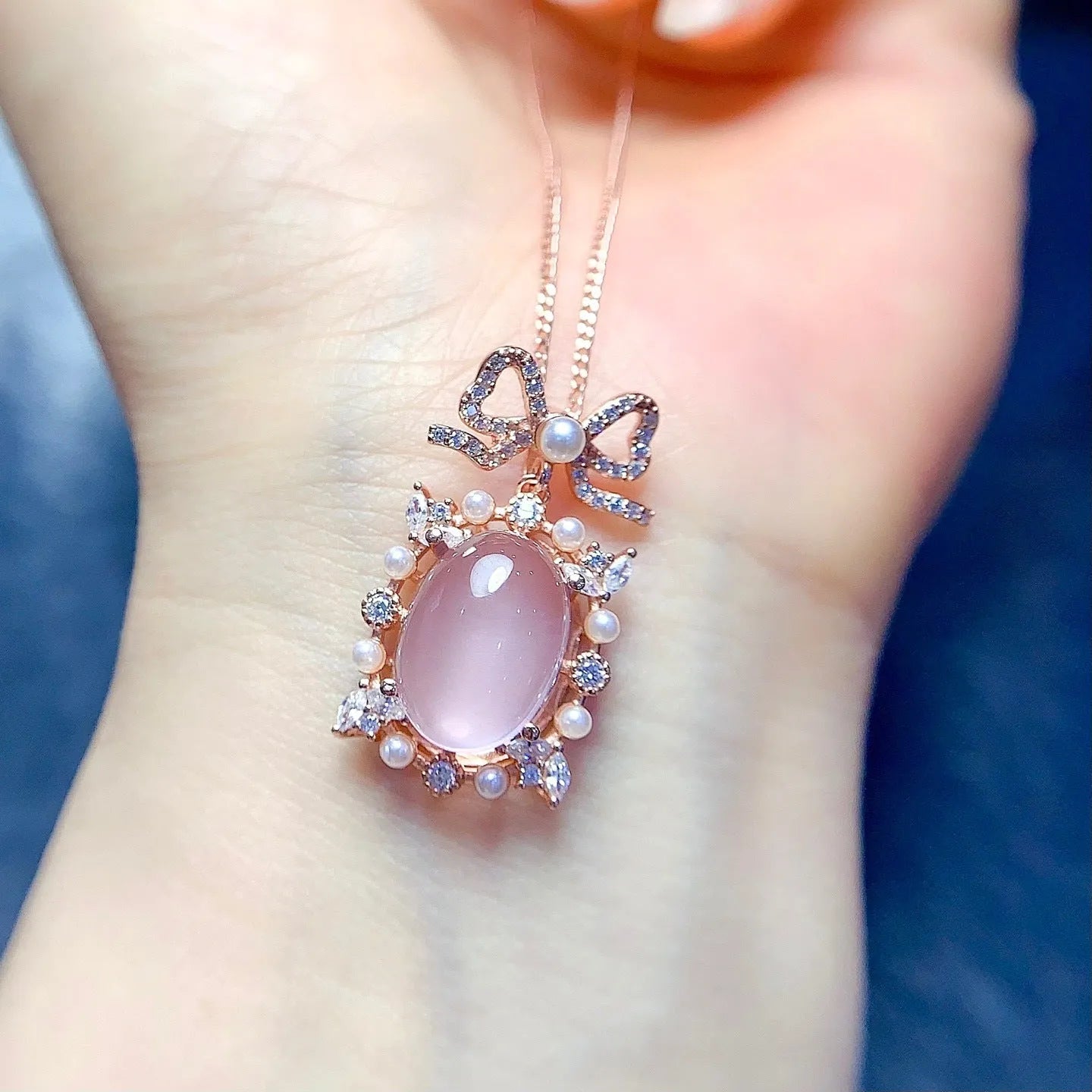 Close-up of a geometric silver pendant with a pink rose quartz stone and rose gold plating on a chain.