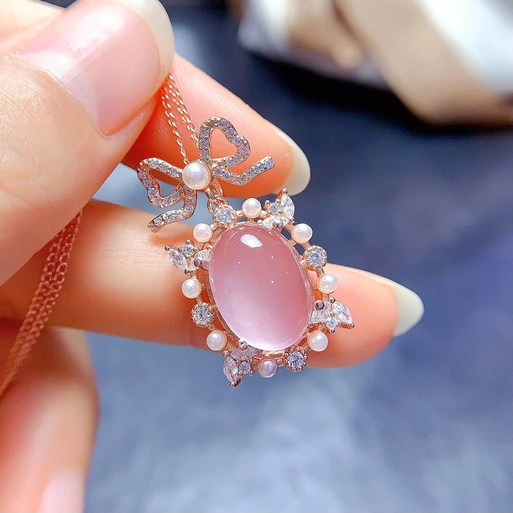 Close-up of a geometric silver pendant with a pink rose quartz stone and rose gold plating on a chain.