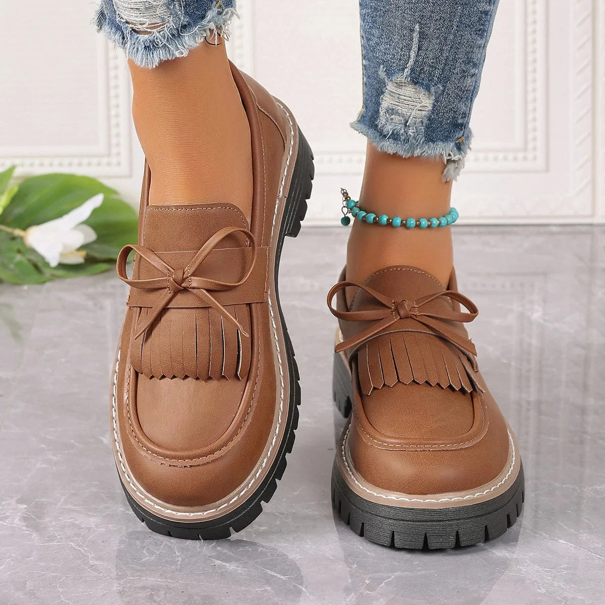 Black and brown women's loafers with tassel and bowknot decoration on a chunky low heel.