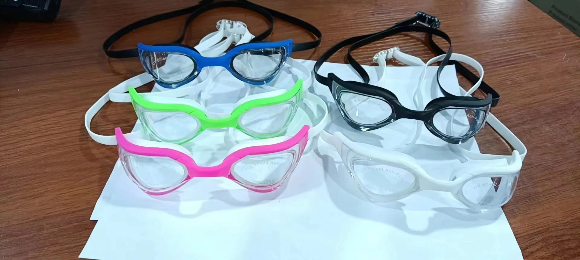 Anti-fog swimming goggles with polycarbonate lenses shown with large and small nose bridges in a plastic mirror box.