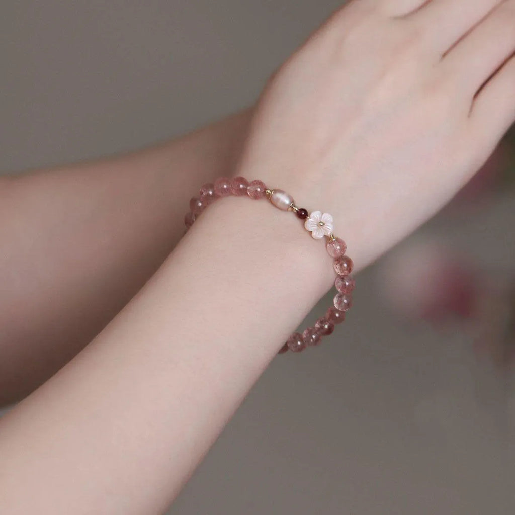 Women's strawberry quartz crystal bracelet with a floral peach blossom design on a wrist.