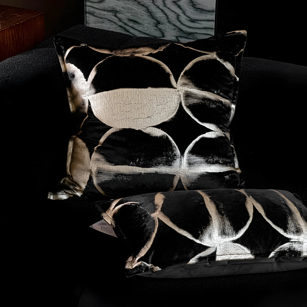 Black and gold abstract patterned flannel sofa cushion with removable cover on a grey sofa.