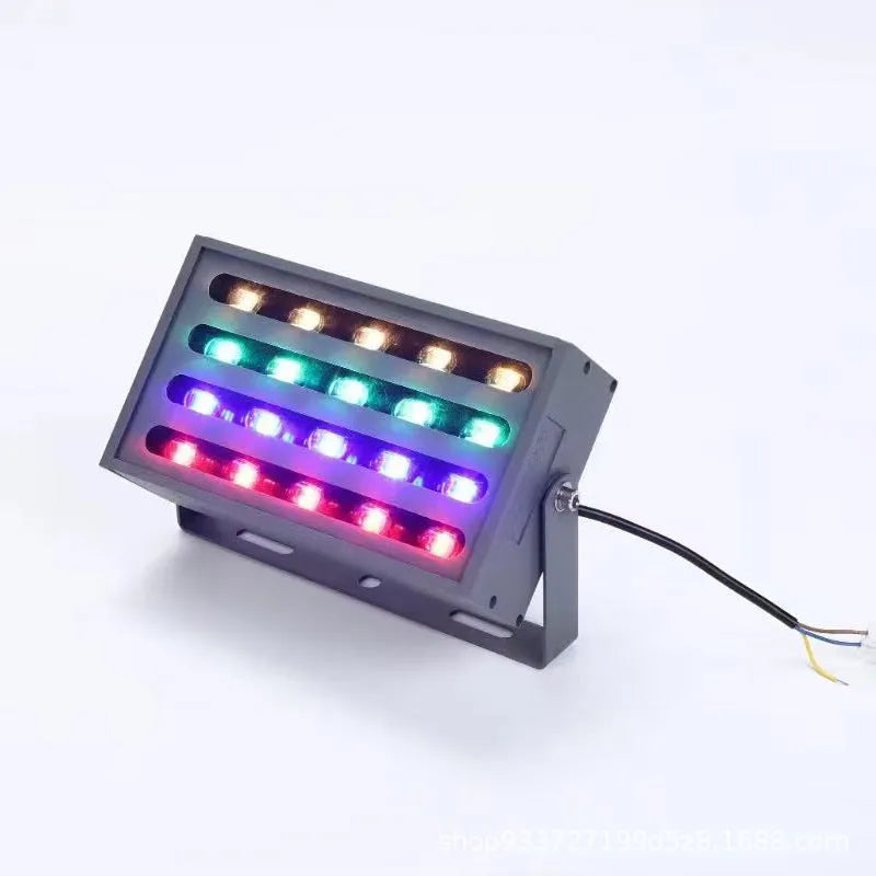 Silver aluminium outdoor LED spotlight projecting multi-coloured light onto trees.
