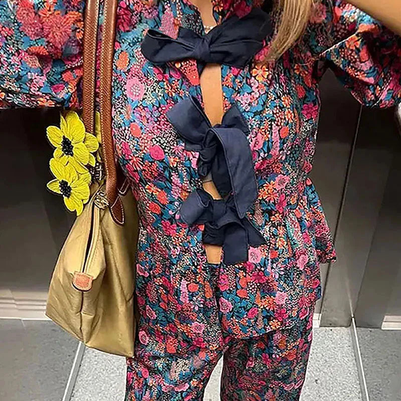 Women's floral print two-piece suit with a tie-neck puff sleeve top and matching trousers.