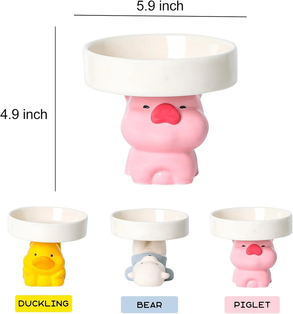 Raised ceramic cat bowl with animal design in pink, yellow, or white on a wooden floor.