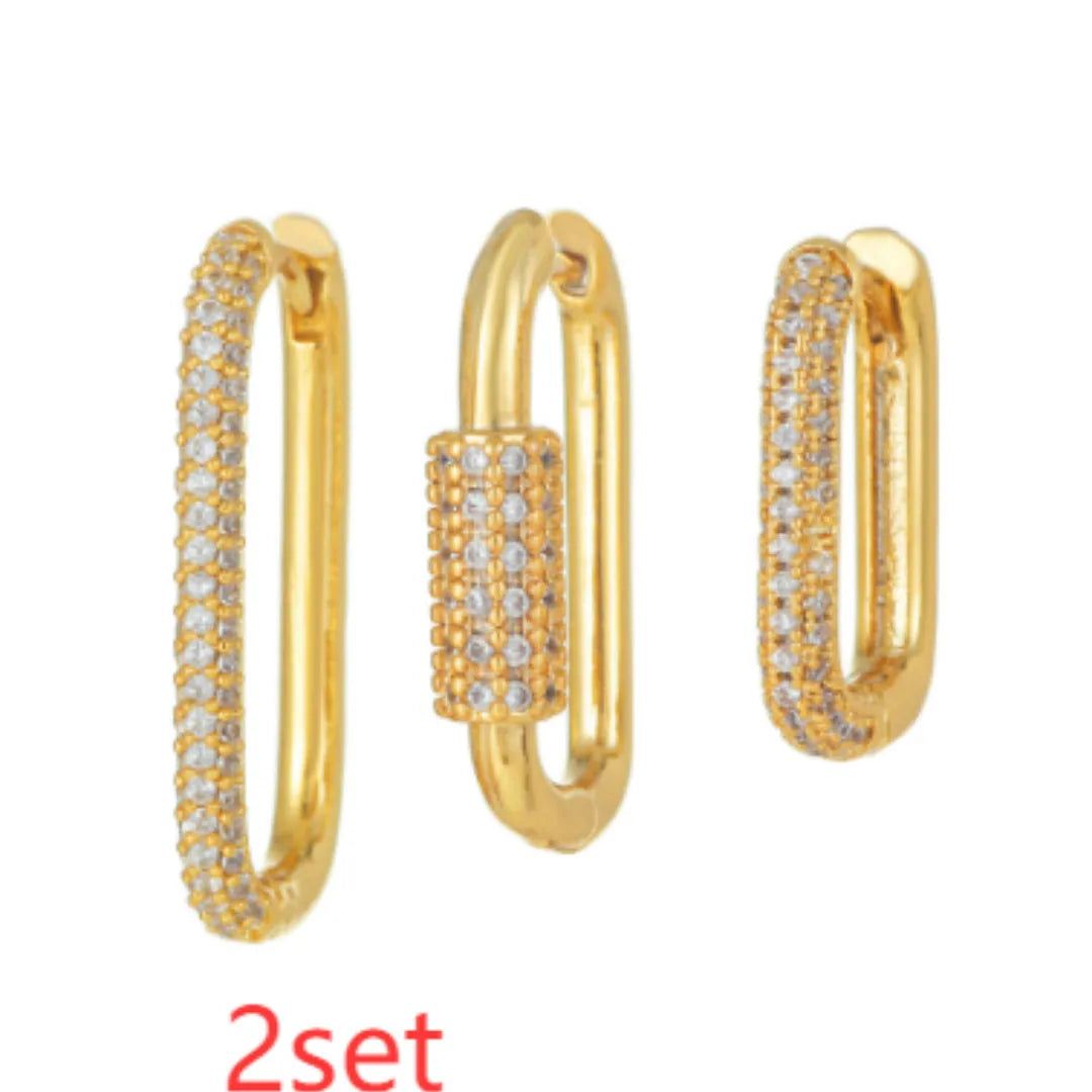 Three geometric square ear clips with inlaid zircon details in gold and white finishes on a grey background.