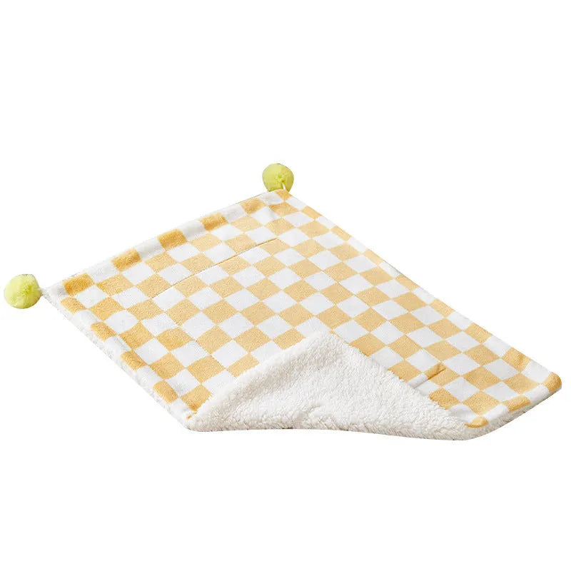 Green plaid pattern pet blanket with fur ball tassels on a sofa.