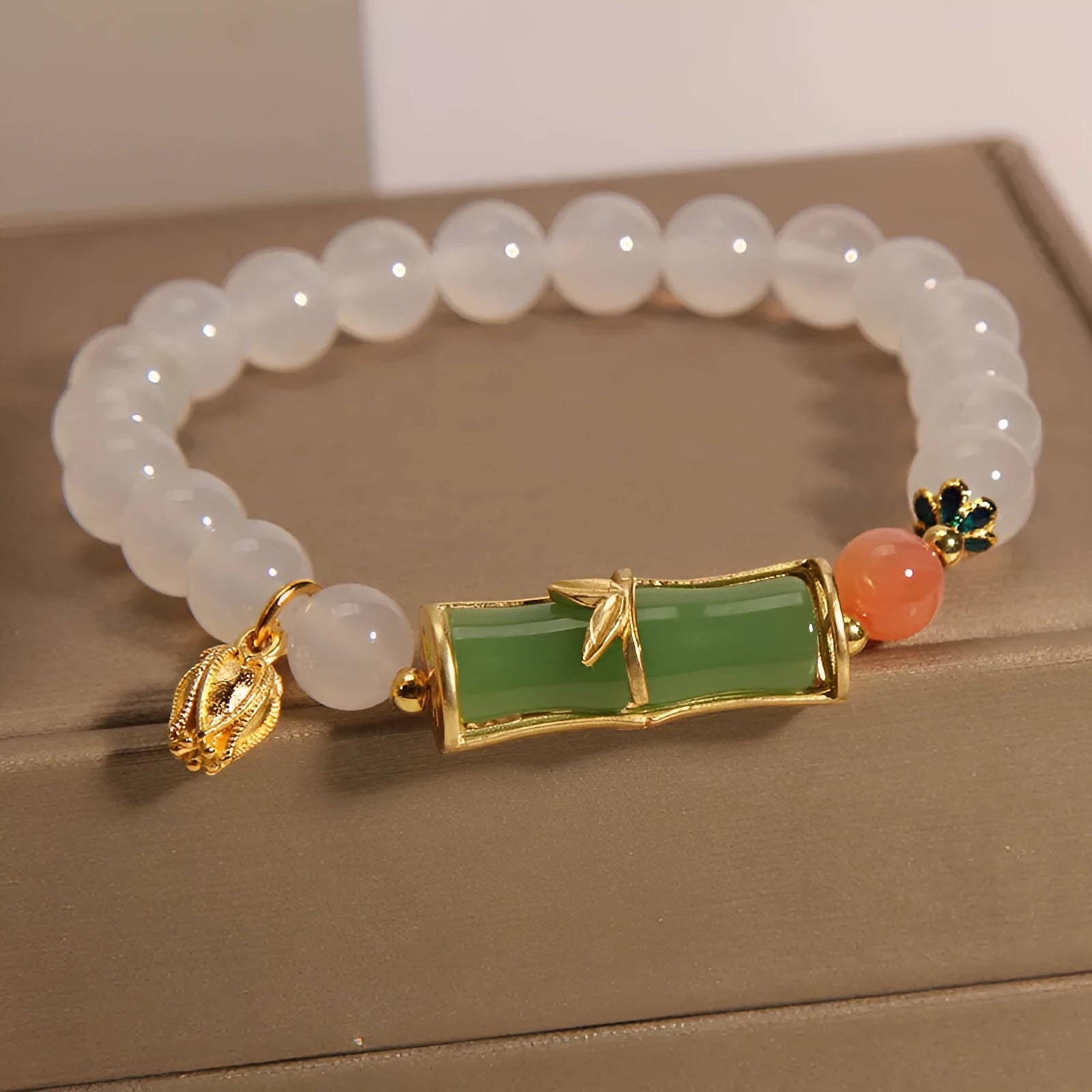 Women's bracelet with white agate bead and bamboo-shaped jade segments on a neutral background.